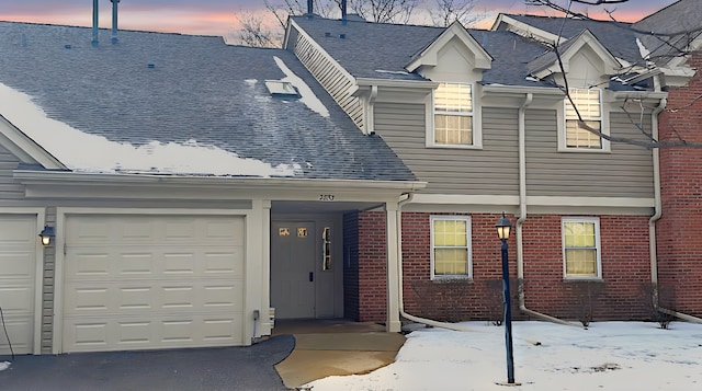 view of front of home with brick siding, roof with shingles, an attached garage, and aphalt driveway