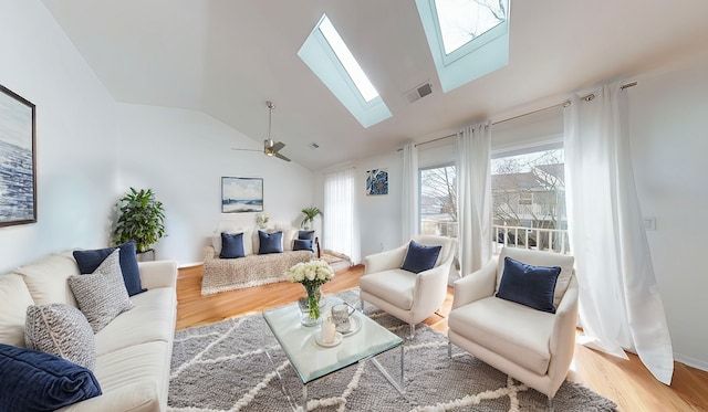 living area with vaulted ceiling with skylight, wood finished floors, visible vents, and a ceiling fan