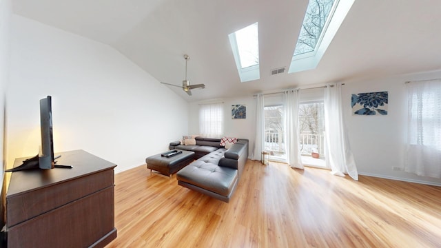 living room with baseboards, vaulted ceiling with skylight, visible vents, and light wood-style floors