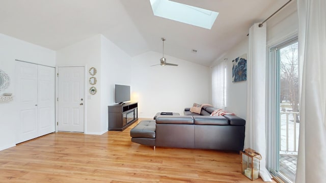 living room featuring lofted ceiling with skylight, visible vents, light wood finished floors, and a ceiling fan