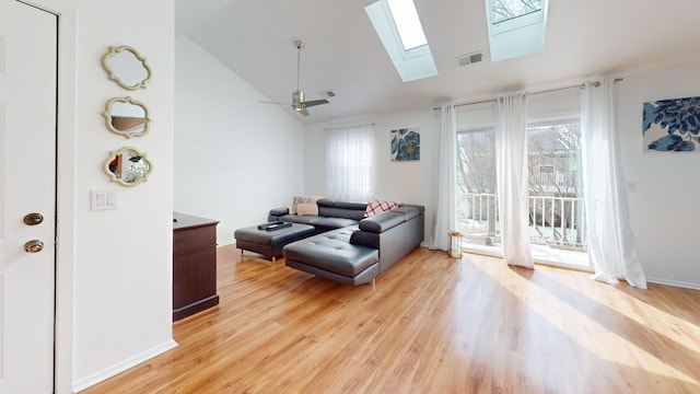 living area featuring a skylight, light wood finished floors, visible vents, baseboards, and ceiling fan