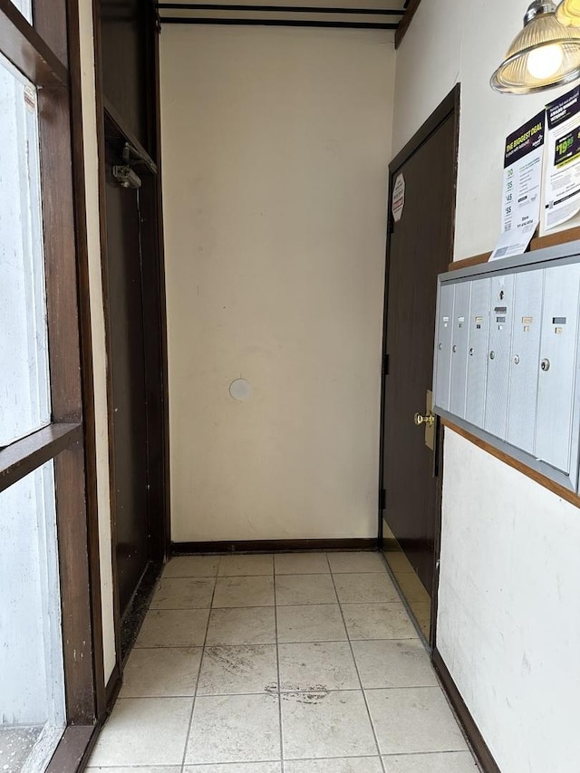 hallway with baseboards, light tile patterned flooring, and mail area