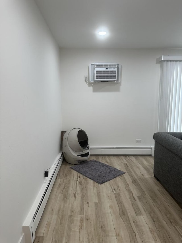 workout room with baseboard heating, a wall unit AC, and light wood-style floors