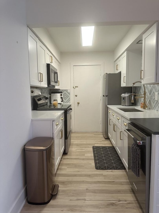 kitchen with light wood-style flooring, a sink, stainless steel appliances, white cabinetry, and backsplash