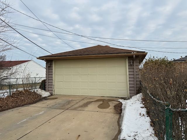 snow covered garage featuring a garage and fence