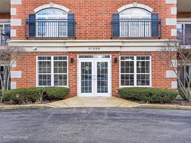 view of exterior entry featuring french doors, a balcony, and brick siding