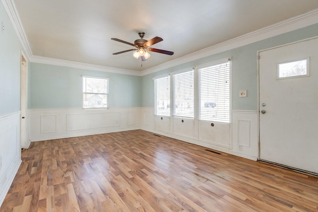 interior space with ornamental molding, a wainscoted wall, ceiling fan, and light wood-style flooring