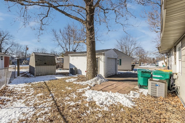 snowy yard featuring a storage shed, central AC, a garage, an outdoor structure, and fence