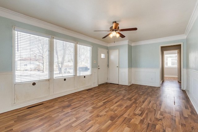 unfurnished room with visible vents, a wainscoted wall, ceiling fan, wood finished floors, and crown molding