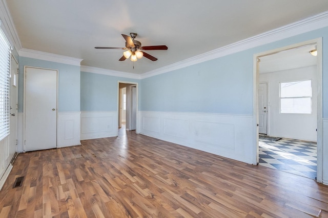 unfurnished room with dark wood-style flooring, crown molding, visible vents, wainscoting, and ceiling fan