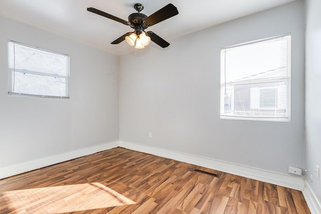 empty room featuring a ceiling fan, visible vents, baseboards, and wood finished floors