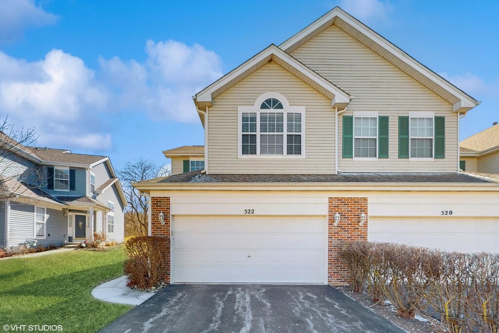 view of front facade featuring an attached garage, aphalt driveway, a front lawn, and brick siding