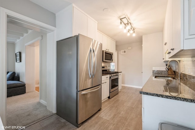 kitchen featuring baseboards, white cabinets, dark stone counters, stainless steel appliances, and a sink