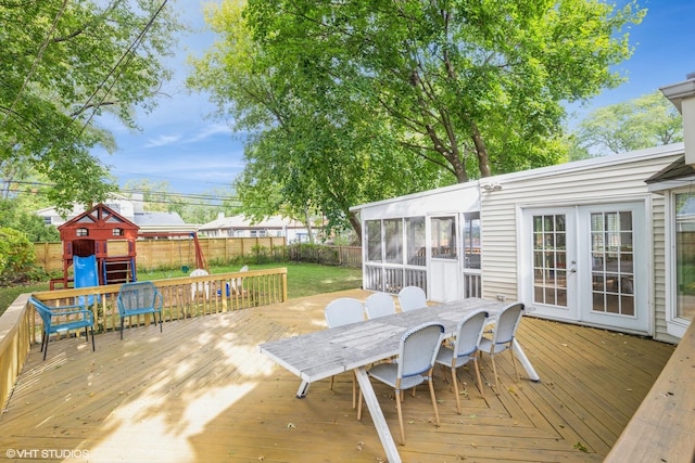 wooden terrace featuring a playground, fence, a sunroom, french doors, and outdoor dining space