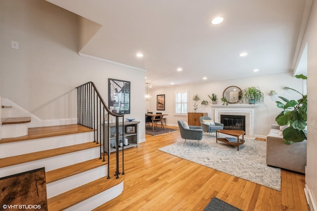 living room featuring recessed lighting, wood finished floors, baseboards, stairway, and a glass covered fireplace