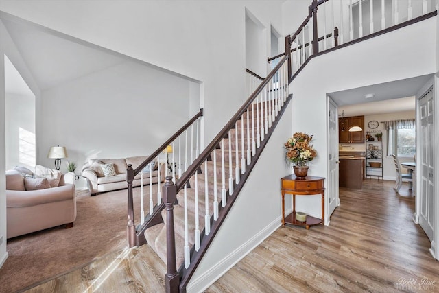 staircase featuring a high ceiling, wood finished floors, and baseboards