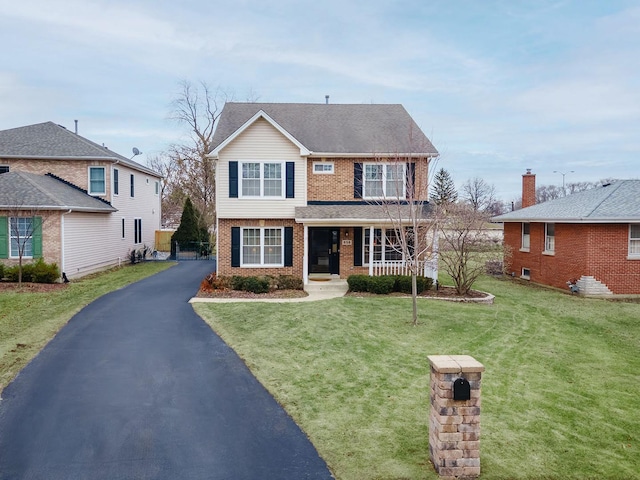 traditional home featuring a porch, brick siding, driveway, and a front lawn