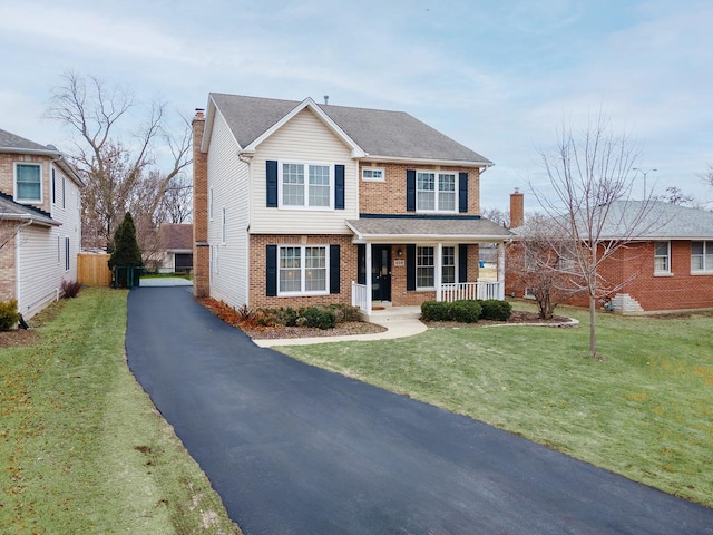 view of front of property featuring aphalt driveway, brick siding, a chimney, a porch, and a front yard