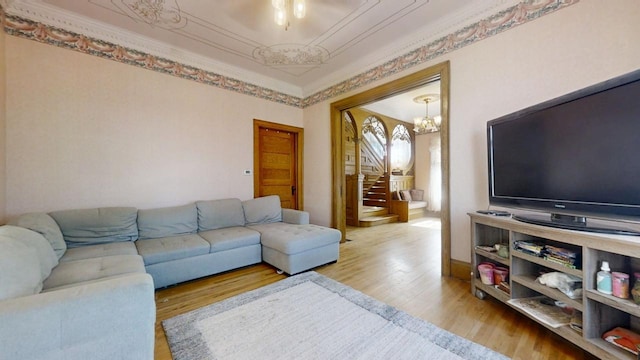 living room featuring stairway, crown molding, a chandelier, and wood finished floors