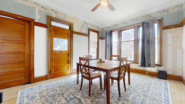 dining space featuring crown molding, a ceiling fan, wood finished floors, baseboards, and wallpapered walls