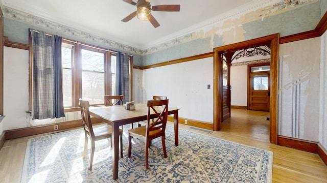 dining space with crown molding, light wood-style floors, a ceiling fan, baseboards, and wallpapered walls