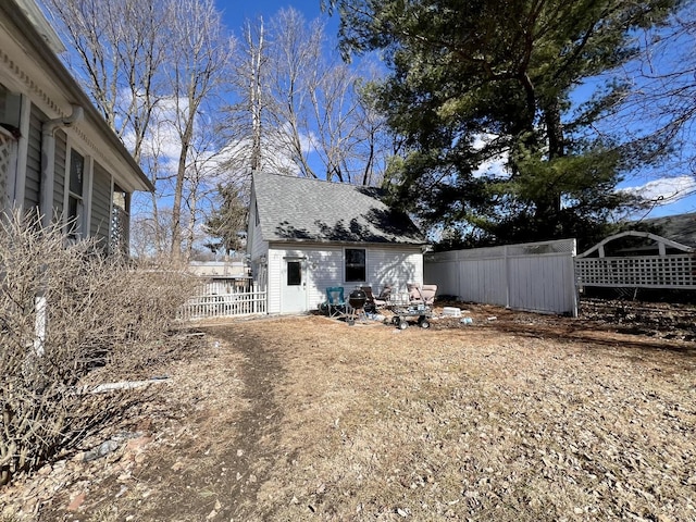 back of house with roof with shingles, an outdoor structure, and fence