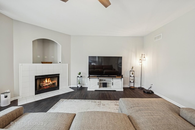 living area featuring a tile fireplace, visible vents, baseboards, and wood finished floors