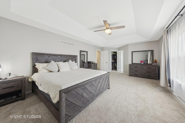 bedroom with a tray ceiling, visible vents, light carpet, ceiling fan, and baseboards