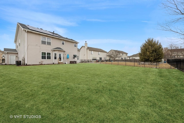 rear view of property with a fenced backyard, roof mounted solar panels, central AC unit, and a yard