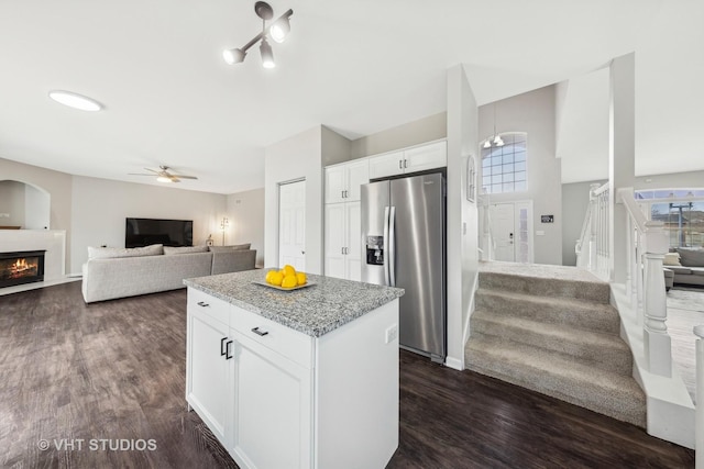 kitchen featuring white cabinets, open floor plan, a lit fireplace, stainless steel fridge with ice dispenser, and a center island