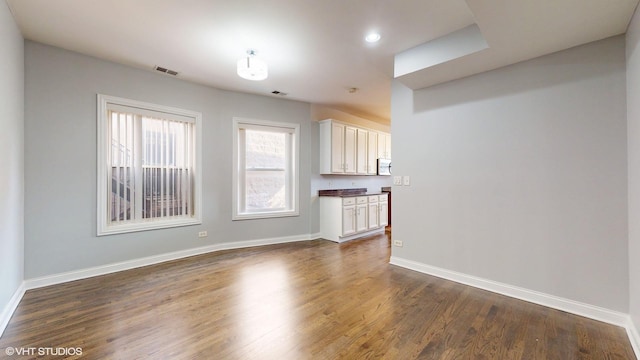 unfurnished living room with dark wood-style flooring, visible vents, and baseboards