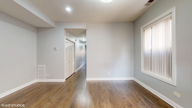 spare room with dark wood-style flooring, visible vents, and baseboards