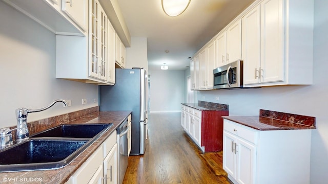 kitchen with dark wood-style floors, appliances with stainless steel finishes, glass insert cabinets, white cabinets, and a sink