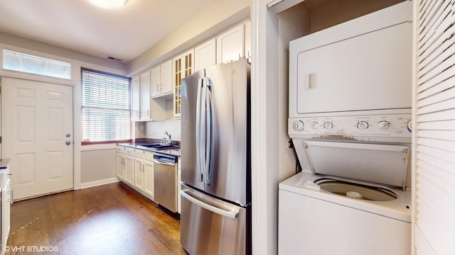 kitchen with appliances with stainless steel finishes, stacked washer / dryer, glass insert cabinets, and white cabinets