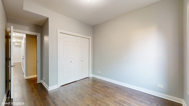 unfurnished bedroom with dark wood-style floors, a closet, and baseboards