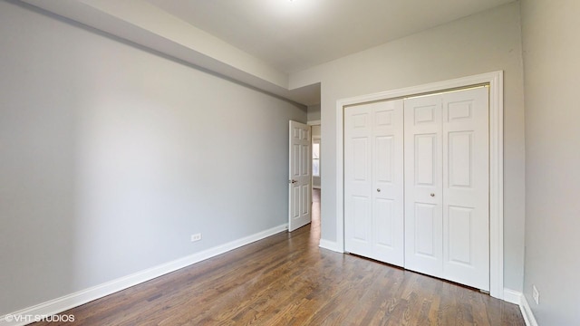 unfurnished bedroom featuring dark wood-type flooring, a closet, and baseboards