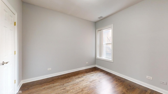 unfurnished room with dark wood-style flooring, visible vents, and baseboards