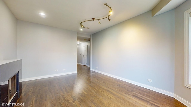 unfurnished living room with dark wood-style flooring, rail lighting, a fireplace, and baseboards