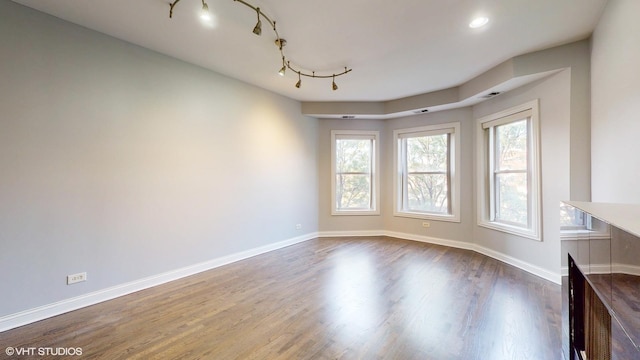 spare room with recessed lighting, wood finished floors, rail lighting, and baseboards