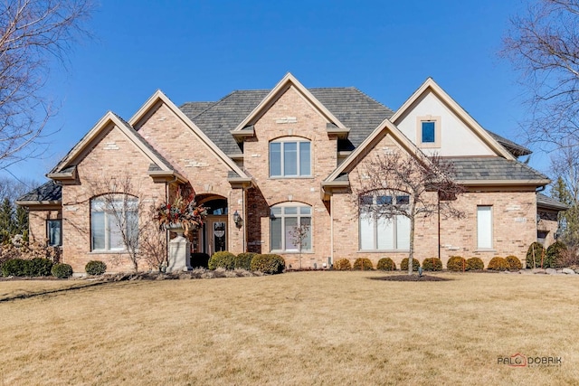 french provincial home featuring a front yard and brick siding