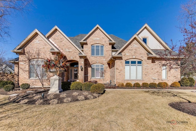 view of front of house featuring brick siding, a front lawn, and roof with shingles