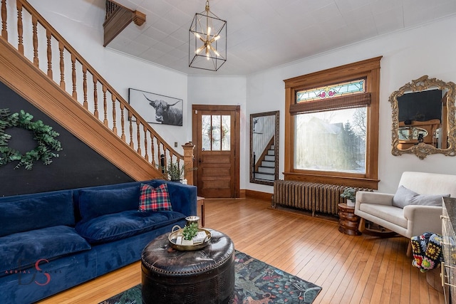 living room with crown molding, radiator, an inviting chandelier, wood finished floors, and stairs