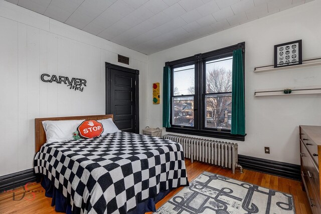 bedroom featuring radiator heating unit, visible vents, and wood finished floors