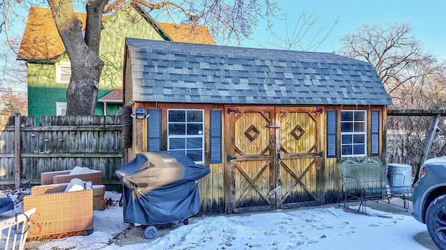 snow covered structure with a storage shed, fence, and an outbuilding