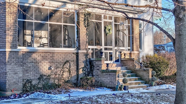 view of snow covered exterior with a sunroom and brick siding