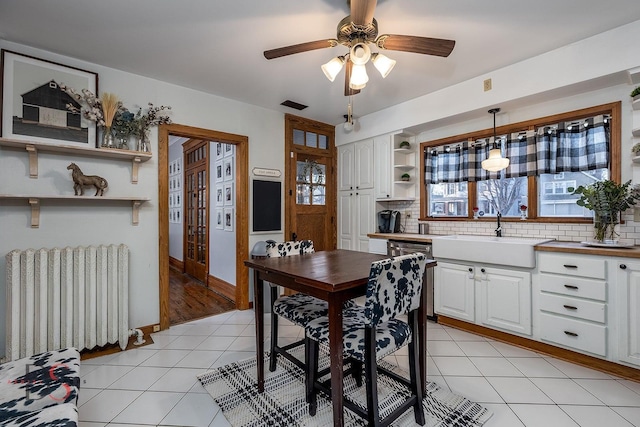 dining area featuring light tile patterned floors, visible vents, radiator heating unit, a ceiling fan, and baseboards