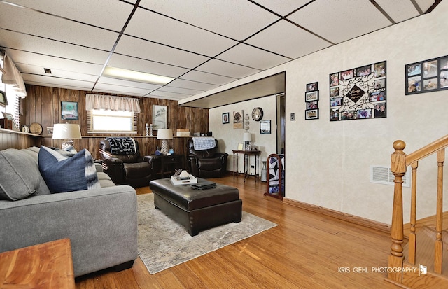 living area with wooden walls, visible vents, stairway, wood finished floors, and a paneled ceiling