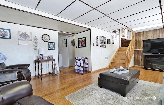 living room featuring a drop ceiling, a fireplace, stairs, and wood finished floors