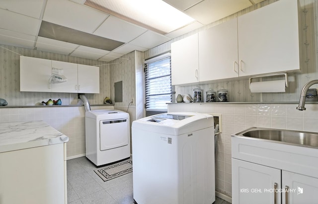 washroom featuring washing machine and dryer, cabinet space, tile walls, and a sink