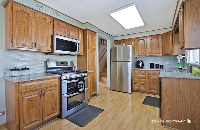 kitchen featuring a sink, appliances with stainless steel finishes, light wood-style flooring, and brown cabinetry